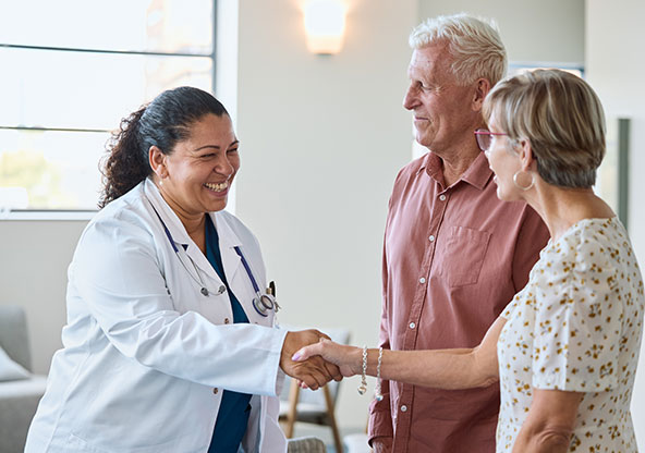 A doctor greets a senior couple with a handshake